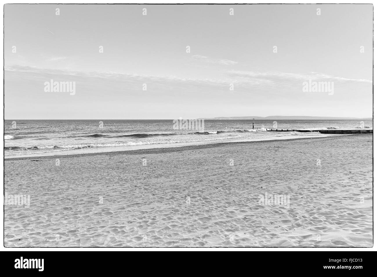 Une image en noir et blanc de la lumière au coucher du soleil d'un pilier à la direction de la mer à la plage de sable et une bande de nuages dans le Banque D'Images