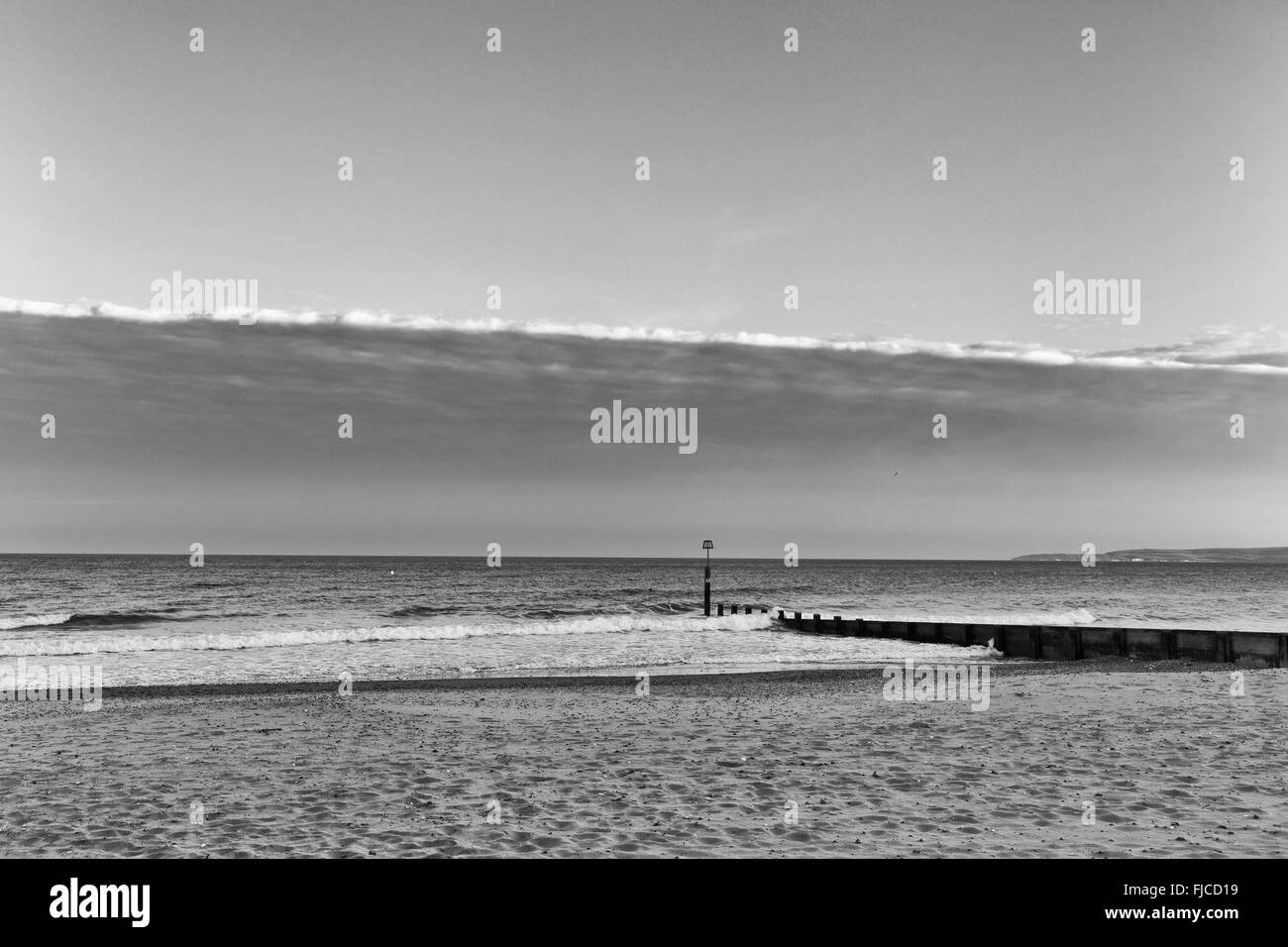 Une image en noir et blanc de lumière au coucher du soleil, d'un pilier à la direction de la mer à la plage de sable et une bande de clo spectaculaire Banque D'Images