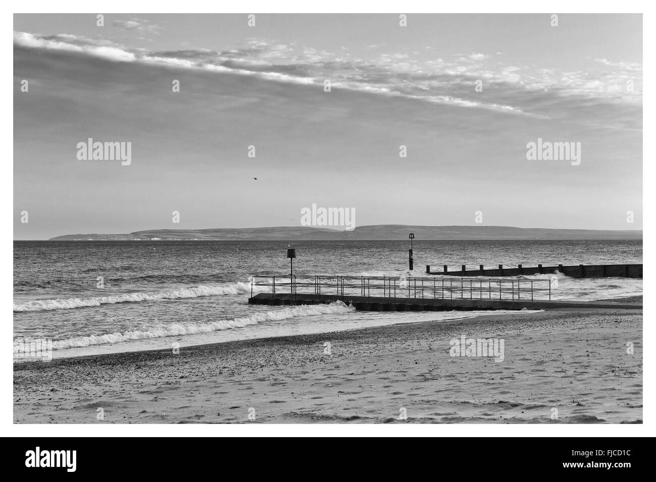 Une image en noir et blanc de la lumière au coucher du soleil d'un pilier à la direction de la mer à la plage de sable et une bande de nuages dans le Banque D'Images