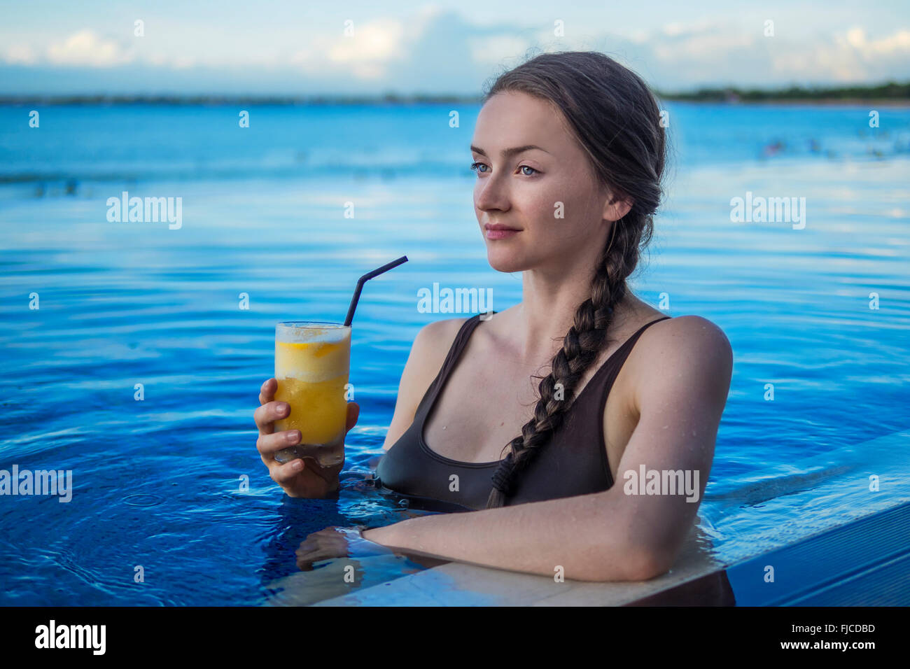 Jeune femme en prenant un verre dans la piscine au coucher du soleil Banque D'Images