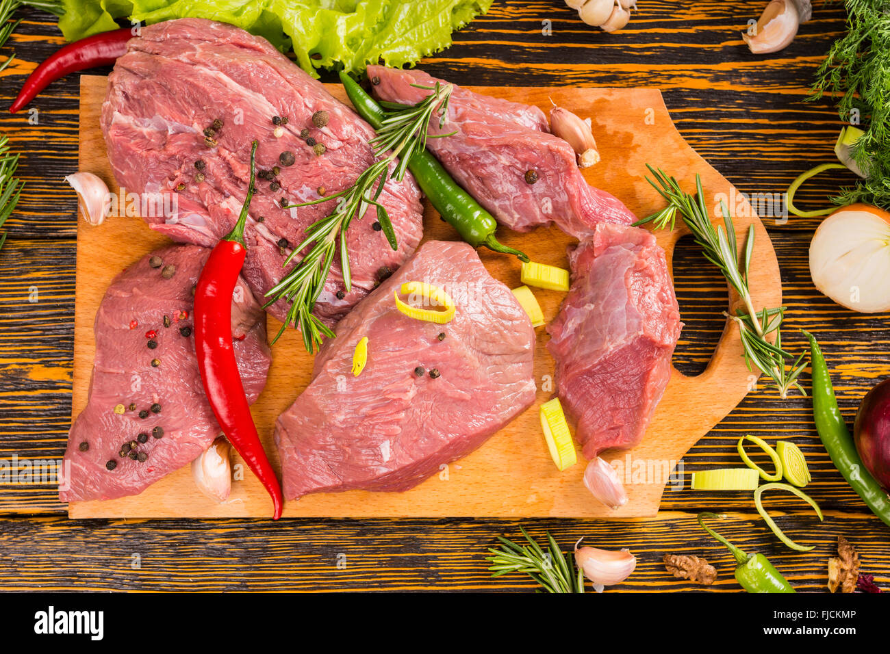 Point de vue du haut vers le bas de la matière première des morceaux de viande rouge avec garniture de poivrons et Rosemary on cutting board prêts à être cuisinés Banque D'Images