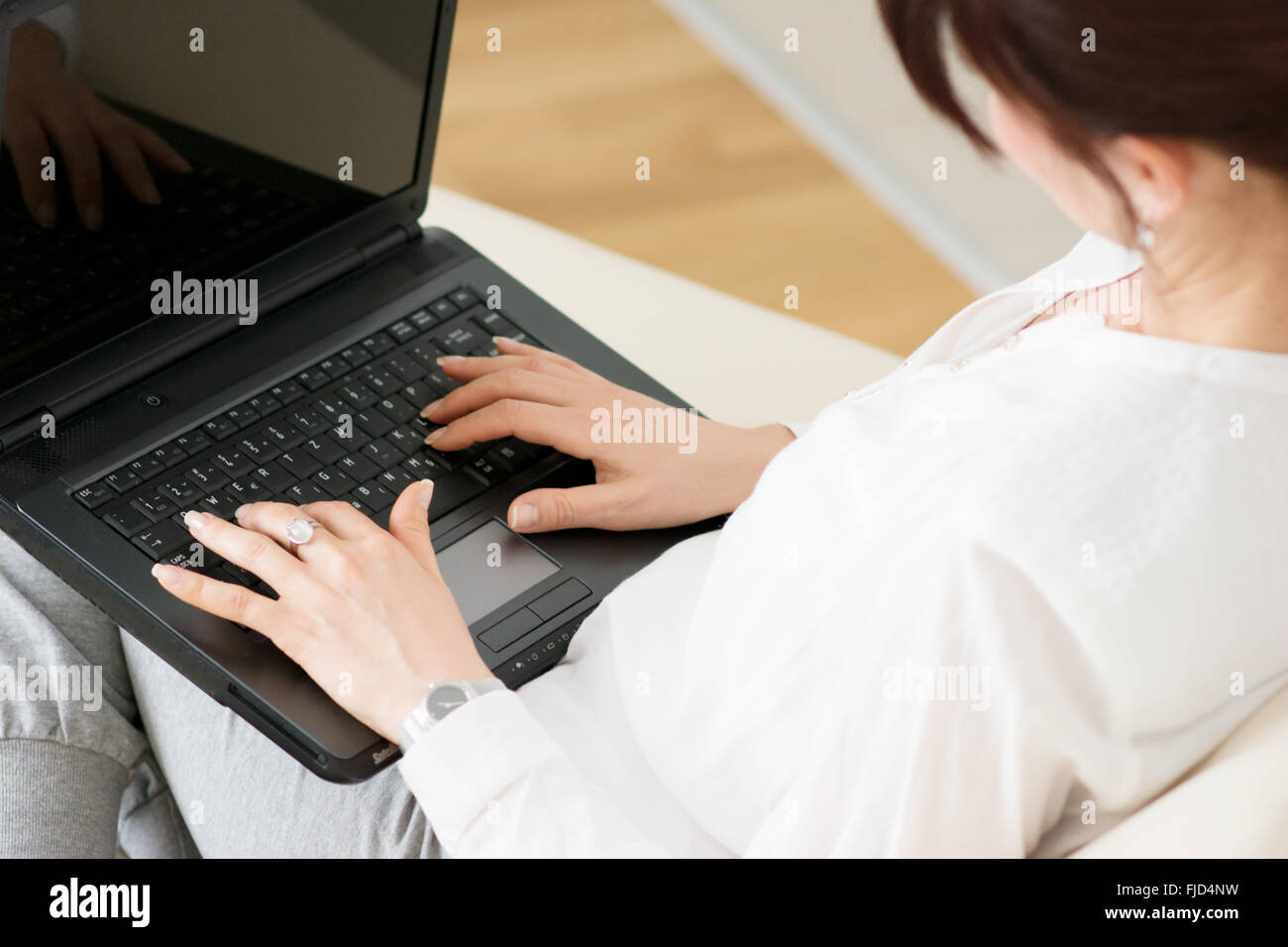 Woman using laptop in sa maison assise sur un sofa Banque D'Images