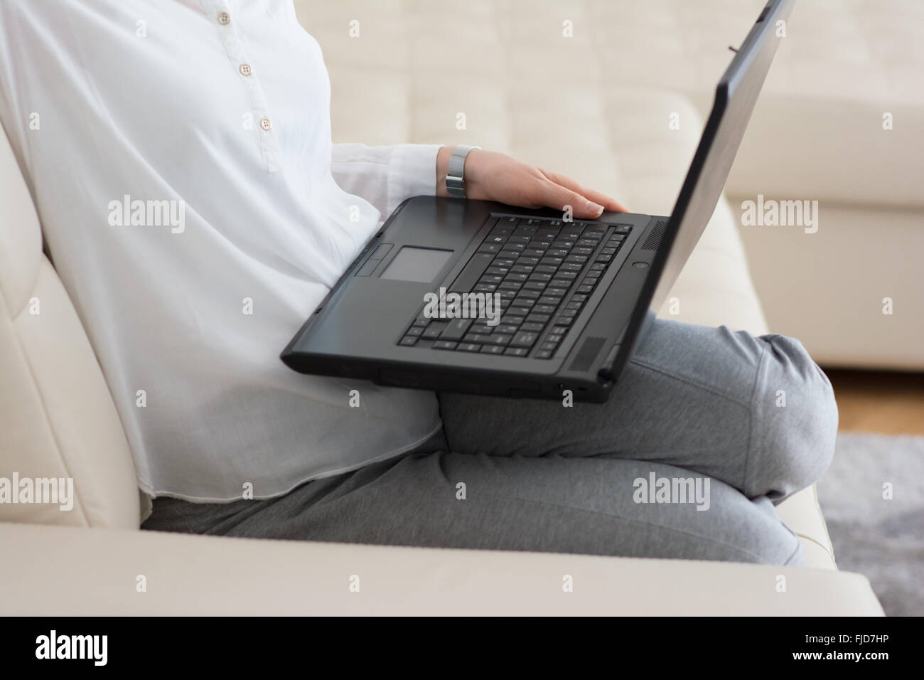Woman using laptop in sa maison assise sur un sofa Banque D'Images