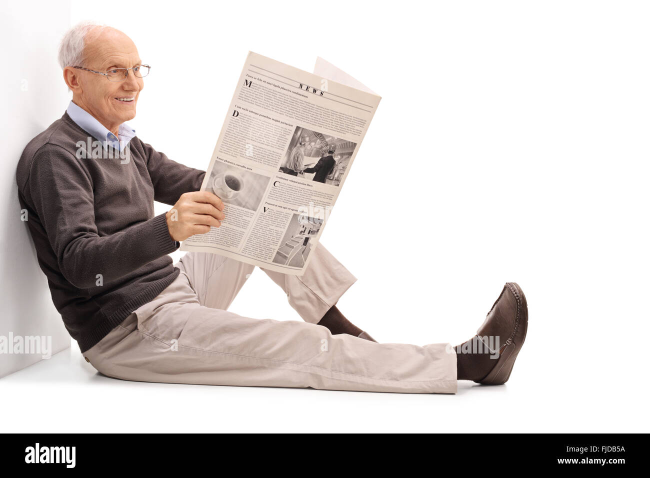 Cheerful senior gentleman lire un journal assis sur le plancher isolé sur fond blanc Banque D'Images