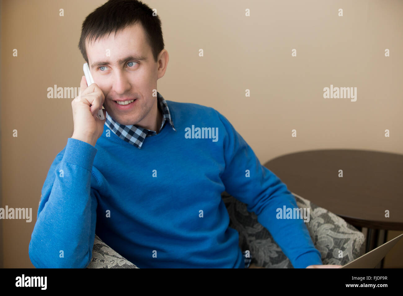 Portrait of attractive occasionnels détendus smiling young man sitting in armchair intérieur, holding cellphone Banque D'Images