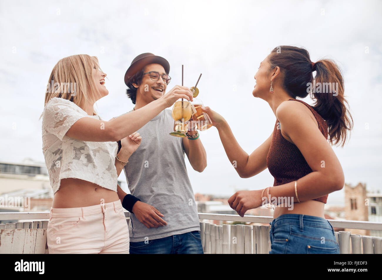 Tourné en plein air de jeunes de prendre un cocktail à l'occasion d'une fête. Trois jeunes friends toasting drinks au cours de soirée sur le toit. Banque D'Images