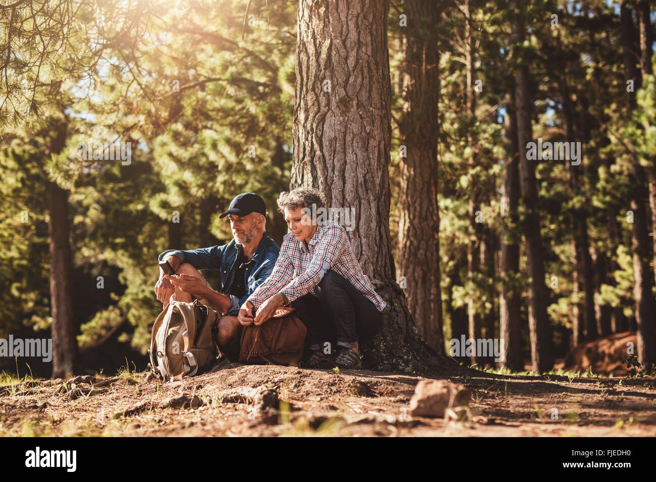 Portrait of mature couple assis sous un arbre avec des sacs et de la boussole. L'homme et de la femme dans la haute forêt. Banque D'Images
