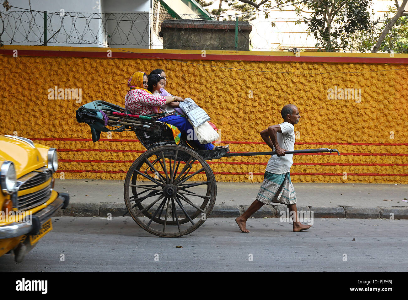 En tirant la main de l'extracteur de pousse-pousse en tirant avec passager passe devant un mur coloré de la rue à Calcutta. Photo de Palash Khan Banque D'Images