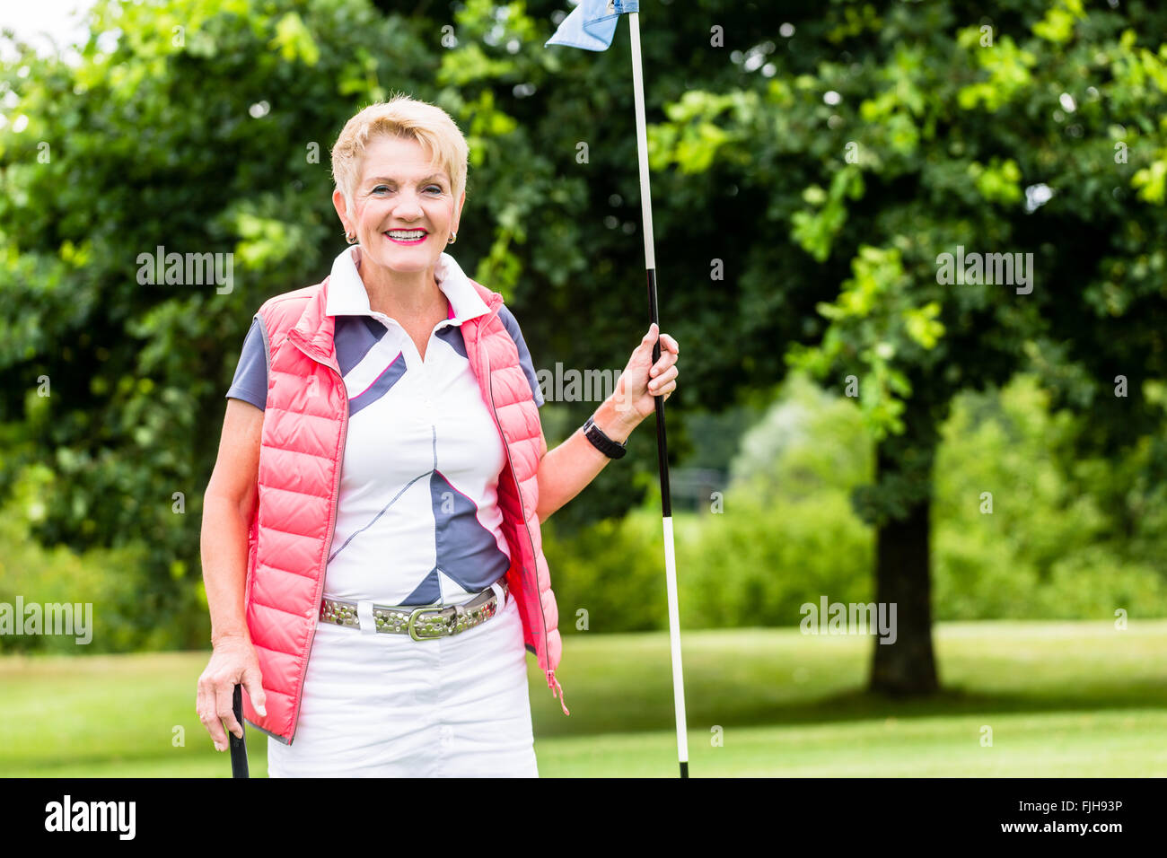Senior woman playing golf on course holding flag Banque D'Images