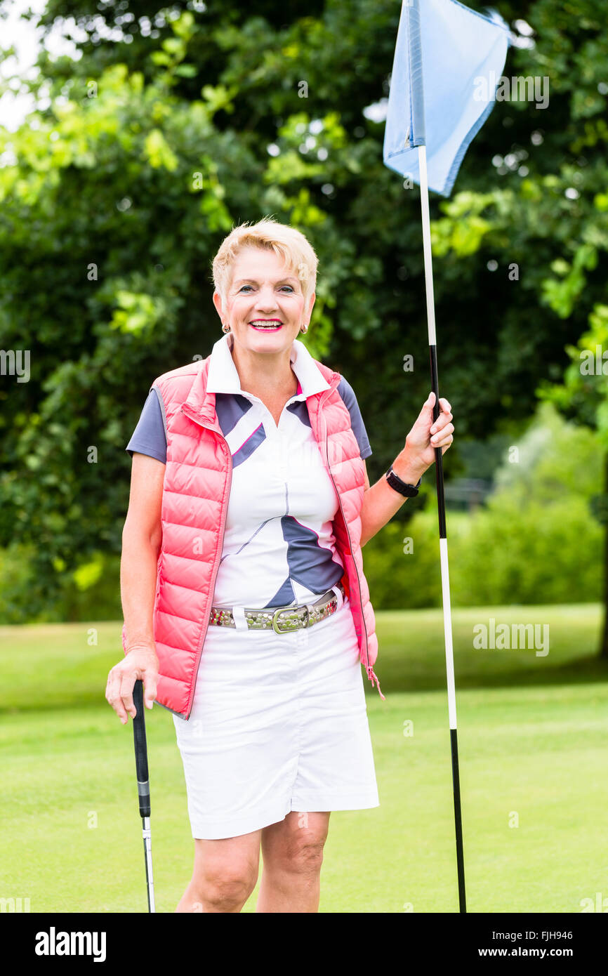 Senior woman playing golf on course holding flag Banque D'Images