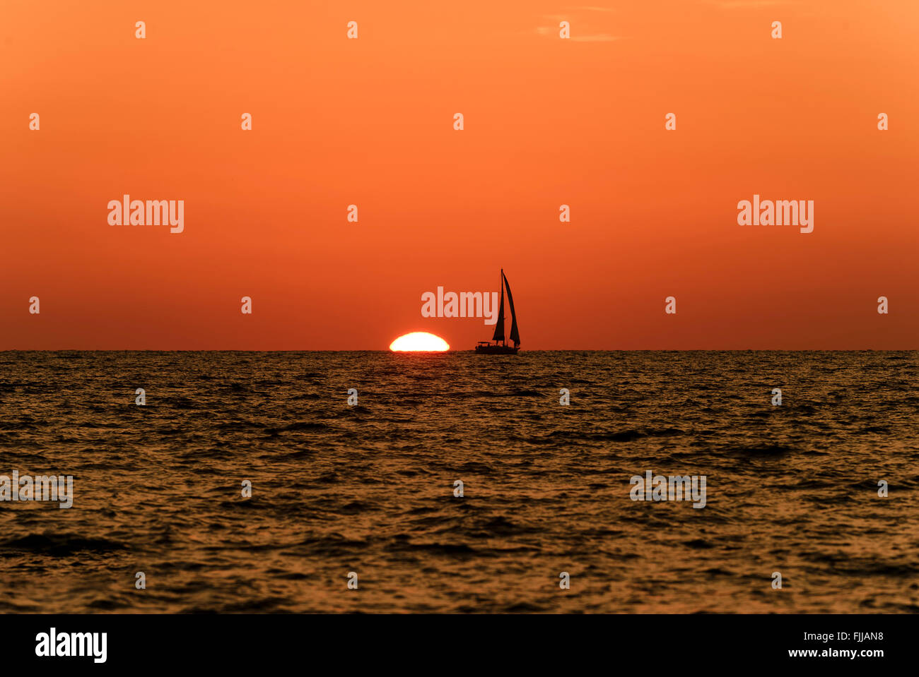 Voilier coucher du soleil est la silhouette d'un voilier avec un blanc chaud brûlant de soleil sur l'océan contre un horizon orange vif Banque D'Images