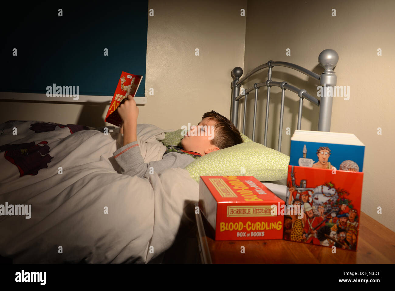 Boy reading 'histoires horribles' book in bed, enfant lire un livre couché dans son lit, l'histoire avant le coucher, lire Banque D'Images