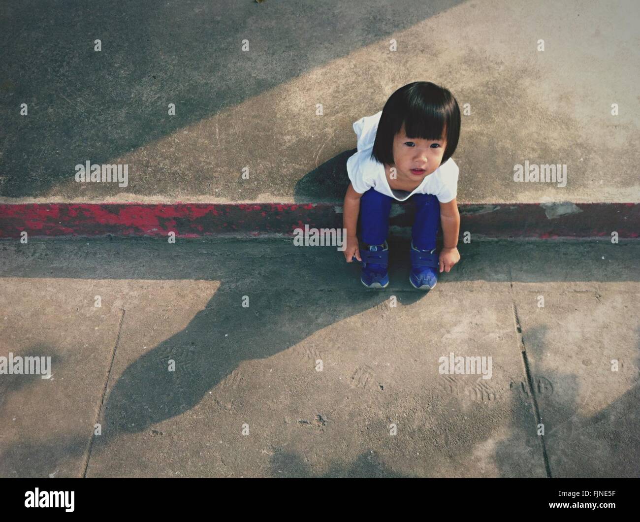 High Angle View of Girl Sitting on Sidewalk Banque D'Images