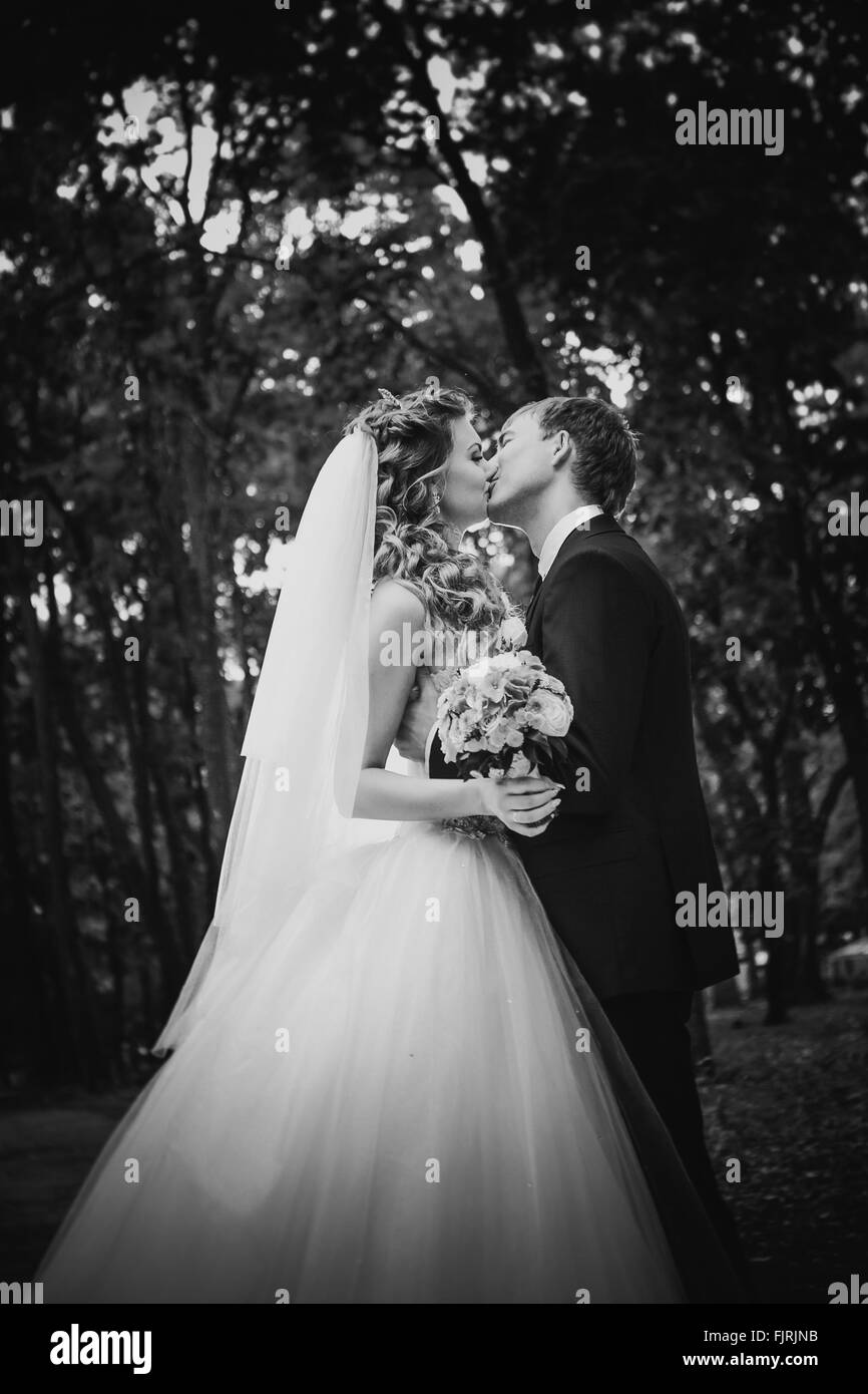 Photographie noir et blanc beau jeune couple posant dans le parc sur un fond d'arbres Banque D'Images