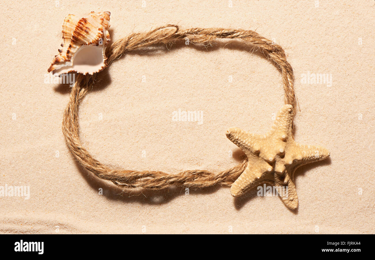 Cadre ovale de corde avec des étoiles de mer et coquillages vides sur le sable. Fond de plage d'été. Vue de dessus Banque D'Images
