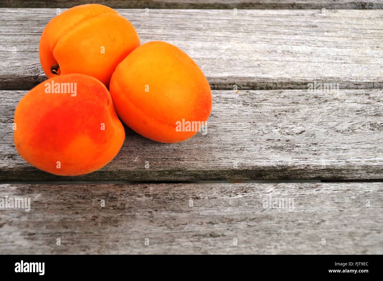 Trois abricots mûrs orange vif sur une table en bois Banque D'Images