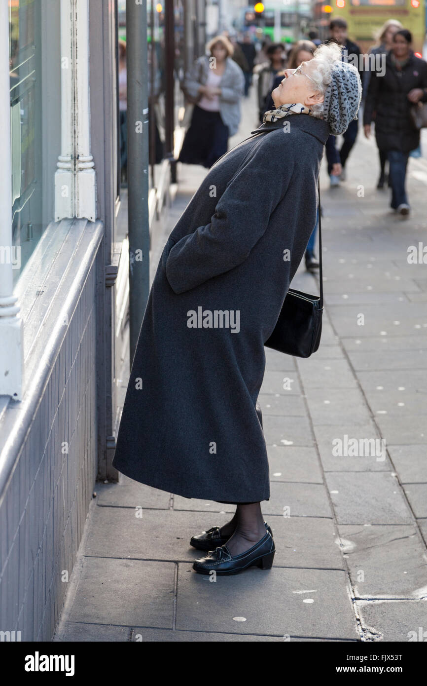 Femme plus âgée se pencher en arrière et à la recherche jusqu'à la partie supérieure de l'affichage de la fenêtre de la boutique. Nottingham, Angleterre, RU Banque D'Images