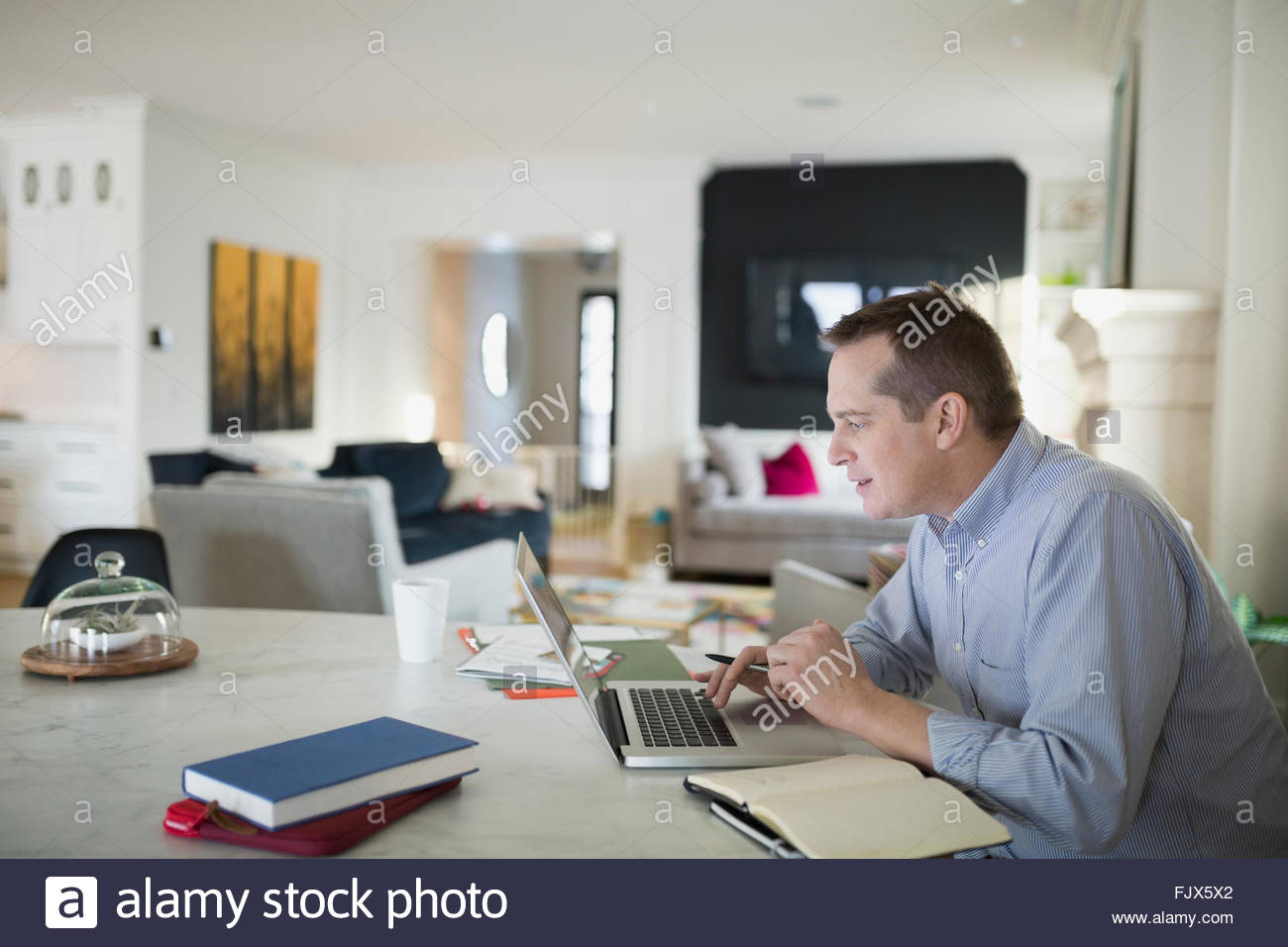 L'homme travaillant à l'ordinateur portable à la table de cuisine Banque D'Images