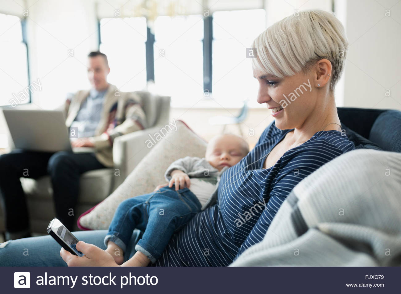 Mother holding baby son et des textos sur canapé Banque D'Images