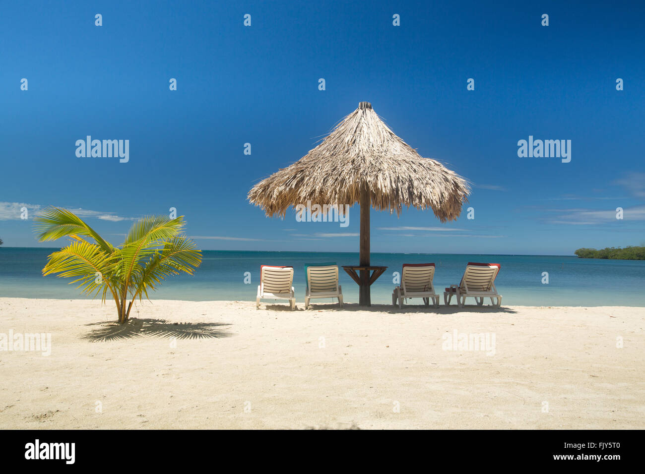 Les palm court à côté de style tiki nuances parapluie vide quatre chaises longues au bord de l'eau de belle blue Caribbean resort Banque D'Images