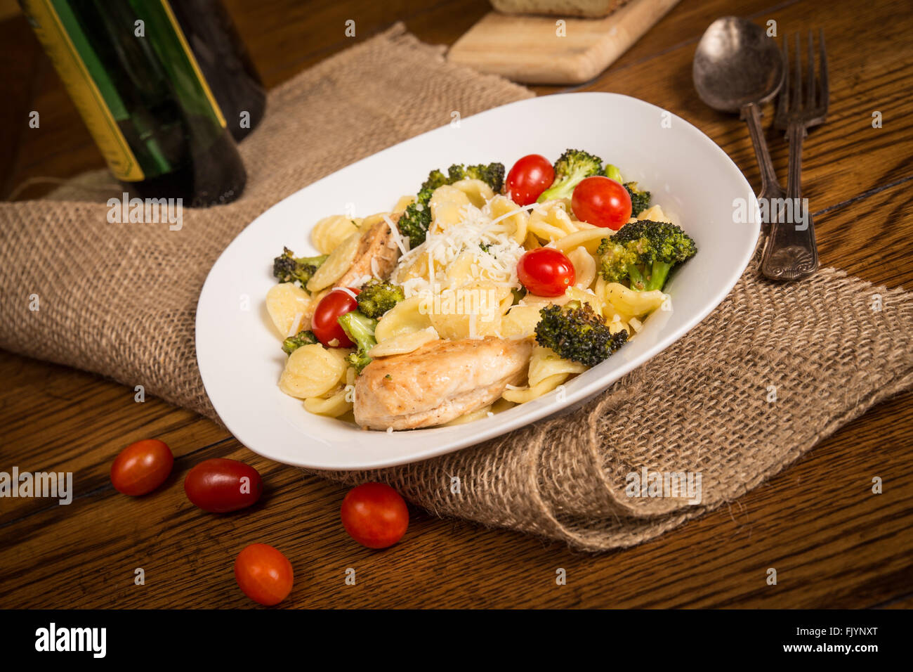 Repas italien authentique avec des pâtes orecchiette, poulet, brocoli, tomates. Miche de pain italien et bouteille de vin dans Banque D'Images