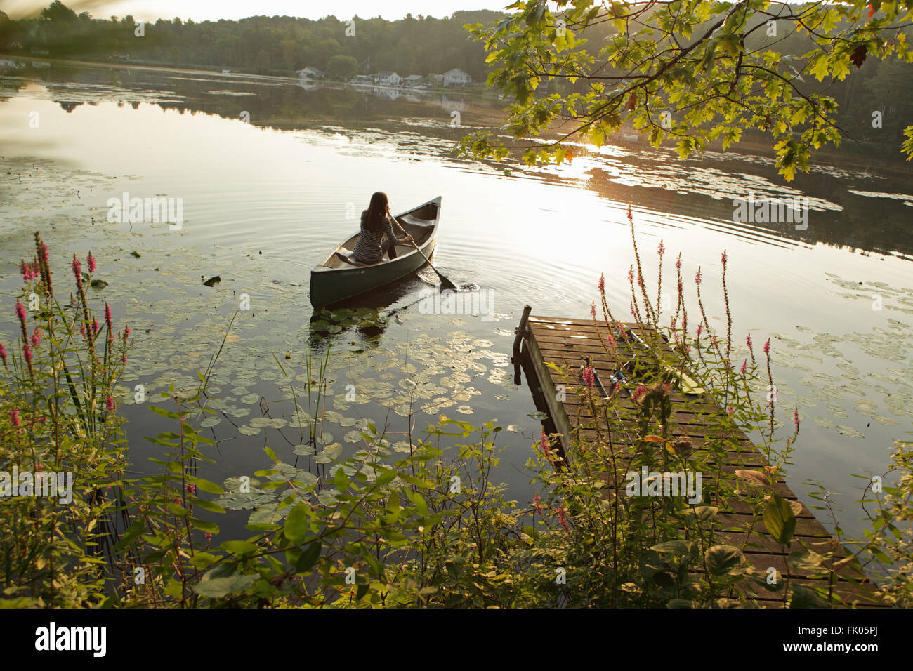 Jeune fille d'une de canots sur le lac Misty, comme le soleil se lève sur une colline lointaine Banque D'Images