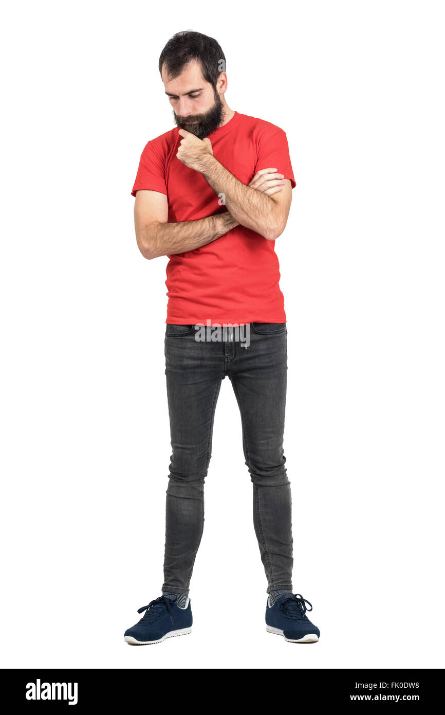 Les jeunes en rouge taille basse t-shirt blanc et barbe caressant la pensée à la recherche vers le bas. La pleine longueur du corps portrait isolated over white Banque D'Images