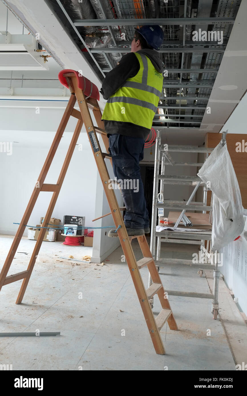 Un électricien travaillant o un ensemble d'étapes dans un plafond nul sur un chantier de construction. Février 2016 Banque D'Images