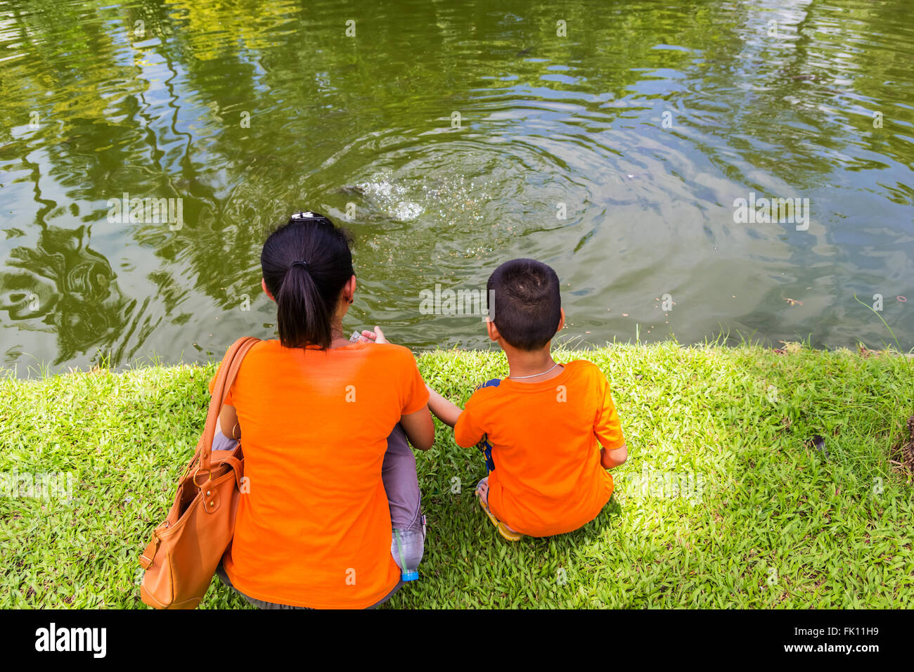 Une photo de la mère et le fils nourrir un poisson près d'un étang Banque D'Images