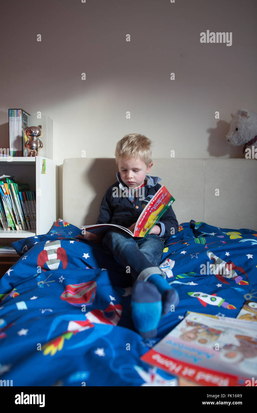 Garçon de 5 ans la lecture dans sa chambre seule à la maison en France Banque D'Images