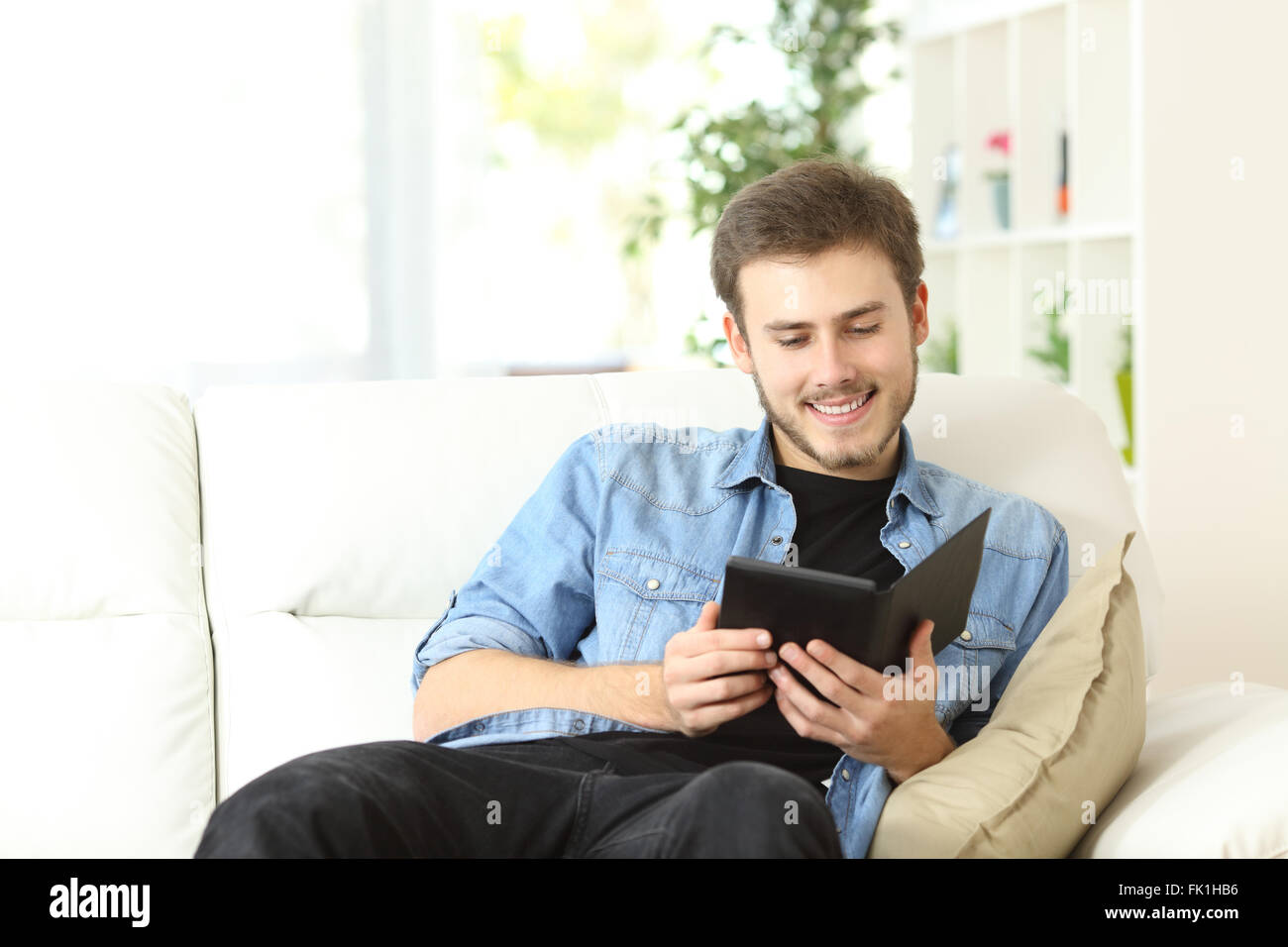 Homme heureux de lire un livre dans un livre électronique Reader assis sur un canapé à la maison Banque D'Images