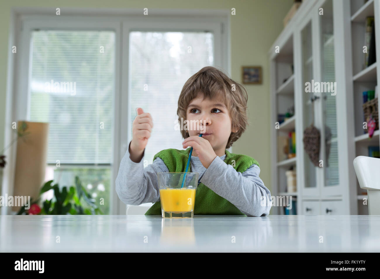 Adorable petit garçon assis à la table de boire le jus d'orange pour le petit déjeuner. Bonne hygiène de vie, la nutrition et la saine alimentation Banque D'Images