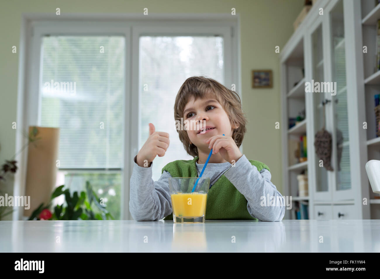 Adorable petit garçon assis à la table de boire le jus d'orange pour le petit déjeuner. Bonne hygiène de vie, la nutrition et la saine alimentation Banque D'Images