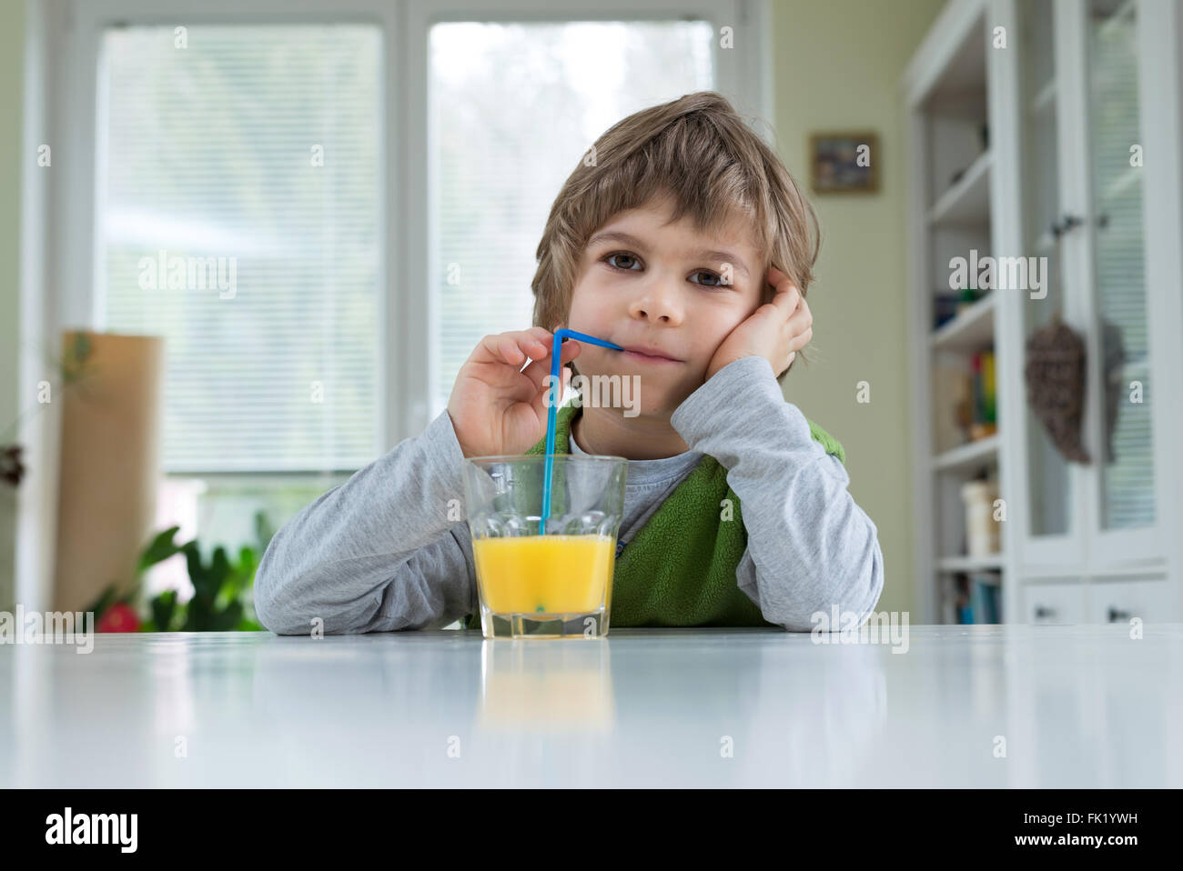 Adorable petit garçon assis à la table de boire le jus d'orange pour le petit déjeuner. Bonne hygiène de vie, la nutrition et la saine alimentation Banque D'Images