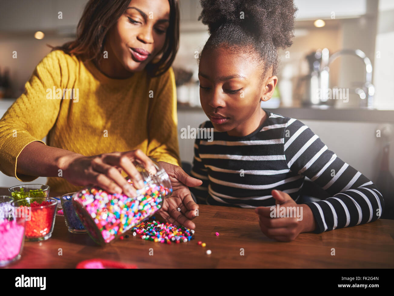 Mère de l'Afrique utile de prendre des perles colorées du conteneur dans la main sur la table en bois pour enfant assis dans la cuisine Banque D'Images