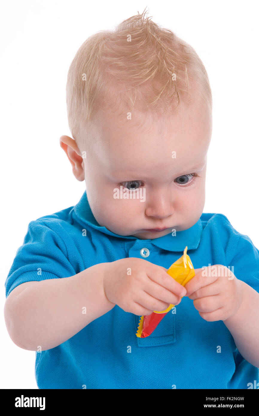 Bébé garçon fait de son mieux pour ouvrir un petit paquet sur fond blanc Banque D'Images