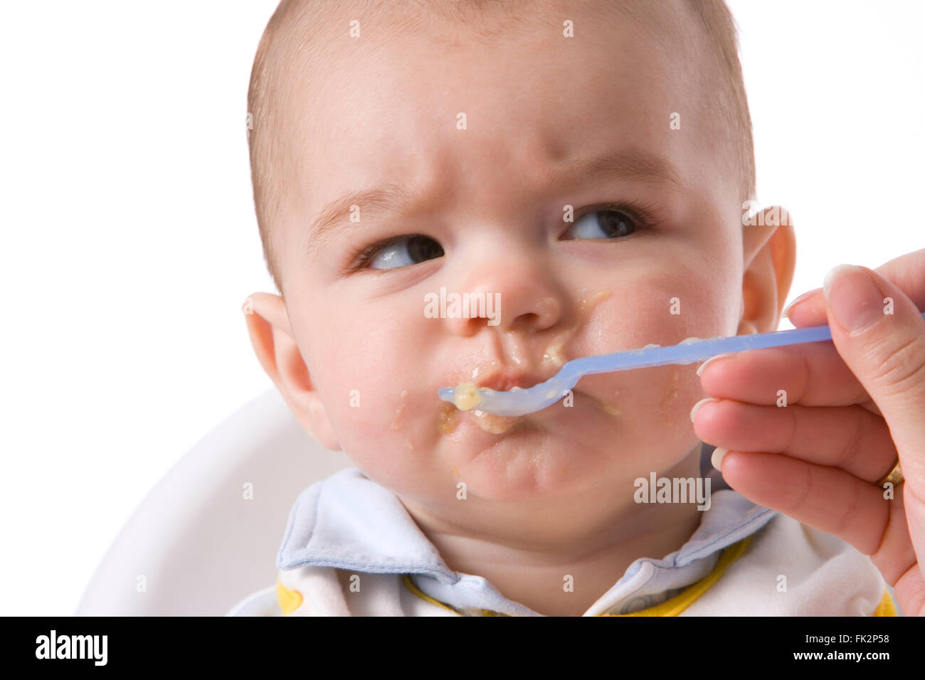 Baby Boy est alimenté avec une cuillère et a une expression désapprobatrice sur fond blanc Banque D'Images