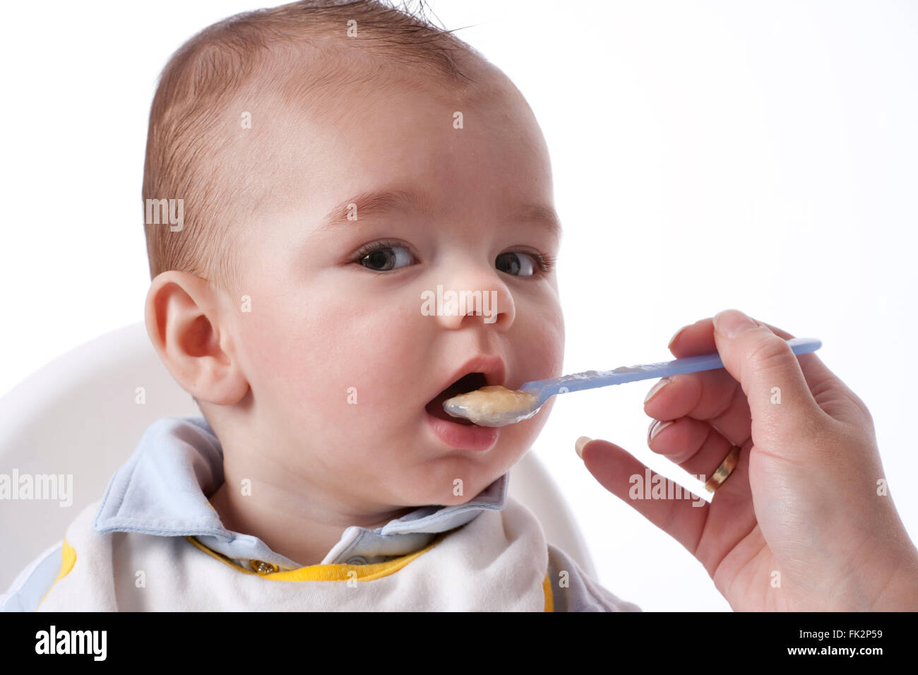 Baby Boy est alimenté avec une cuillère sur fond blanc Banque D'Images