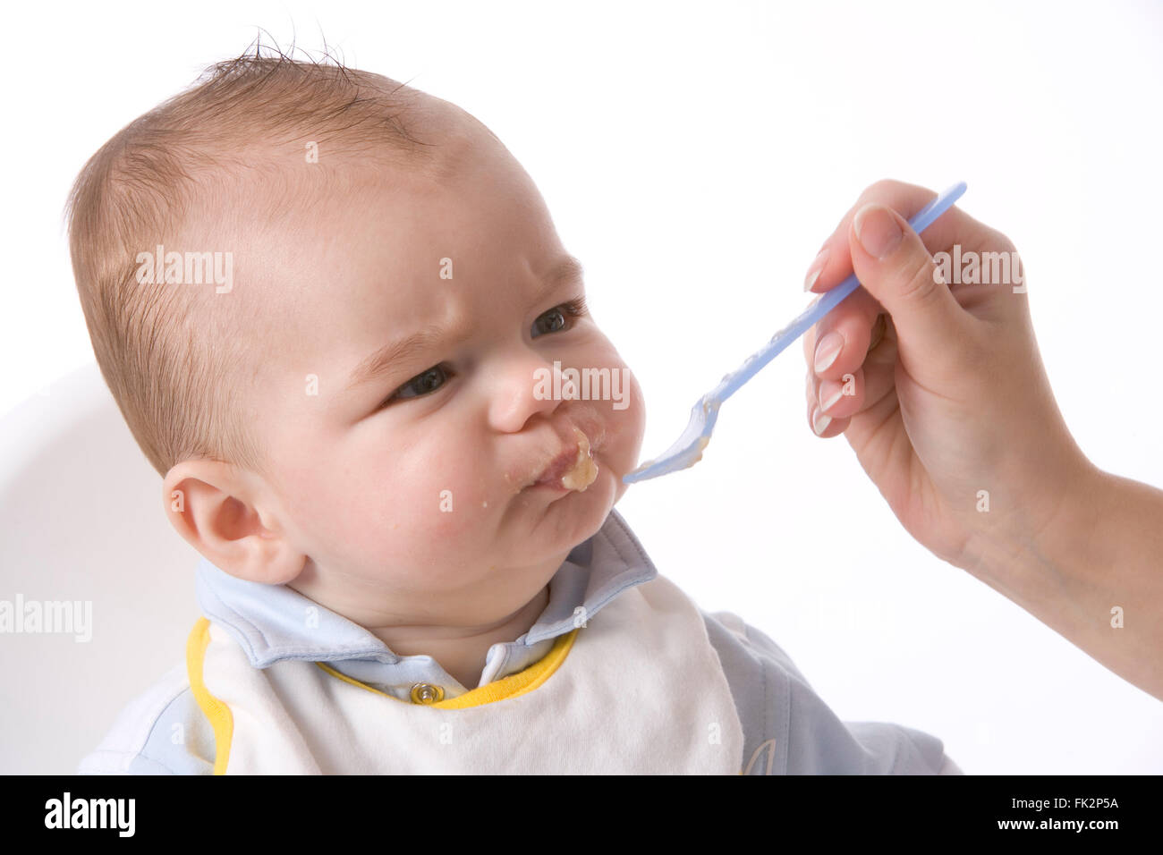 Baby Boy est alimenté avec une cuillère et a une expression désapprobatrice sur fond blanc Banque D'Images