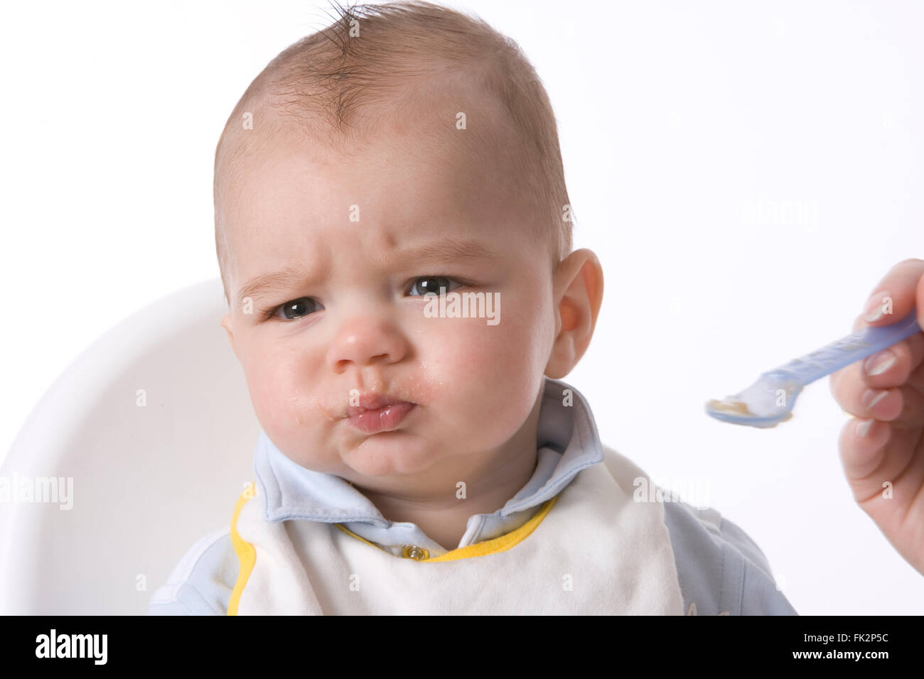 Baby Boy est alimenté avec une cuillère et a une expression désapprobatrice sur fond blanc Banque D'Images