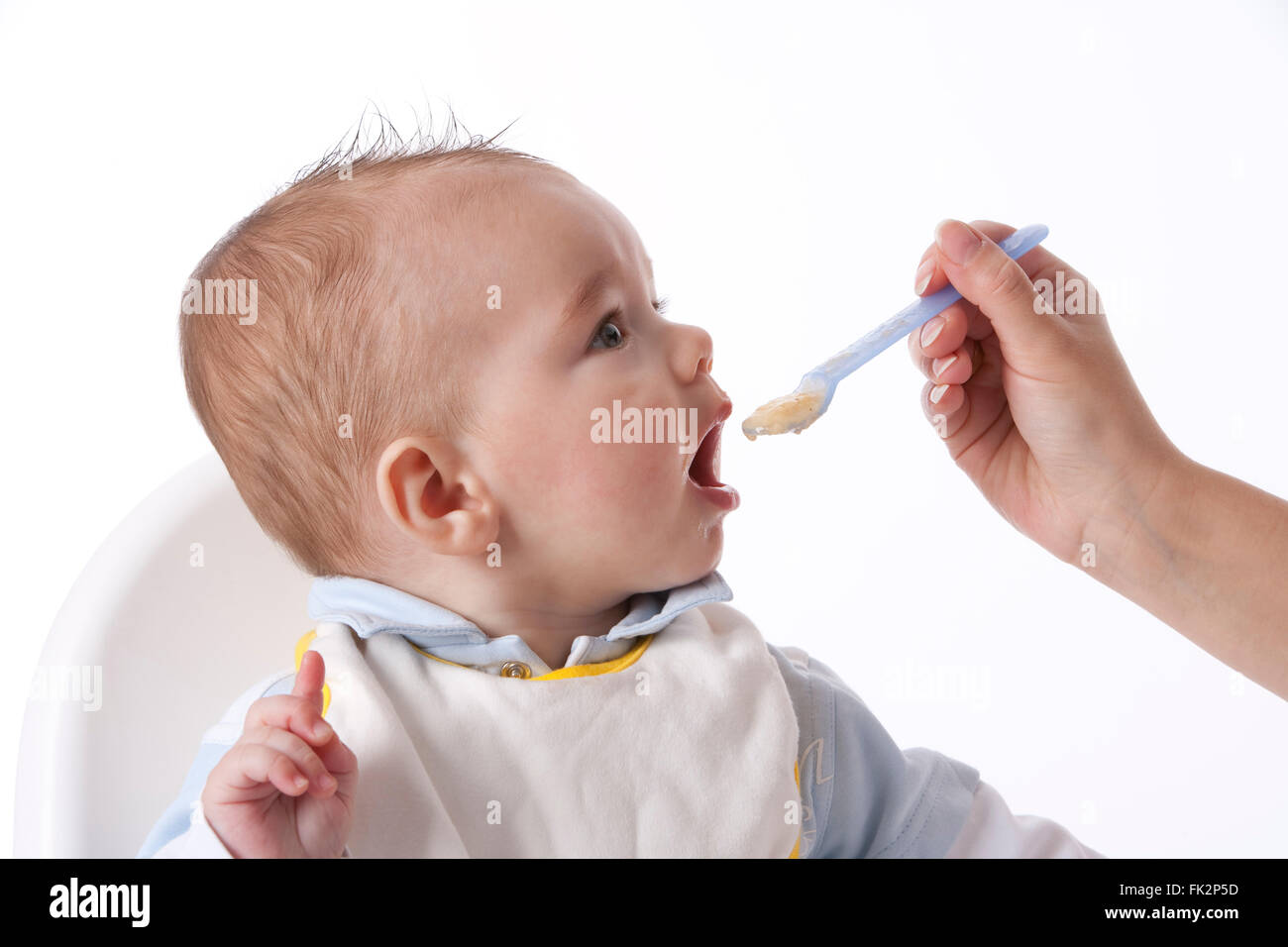 Baby Boy est alimenté avec une cuillère sur fond blanc Banque D'Images