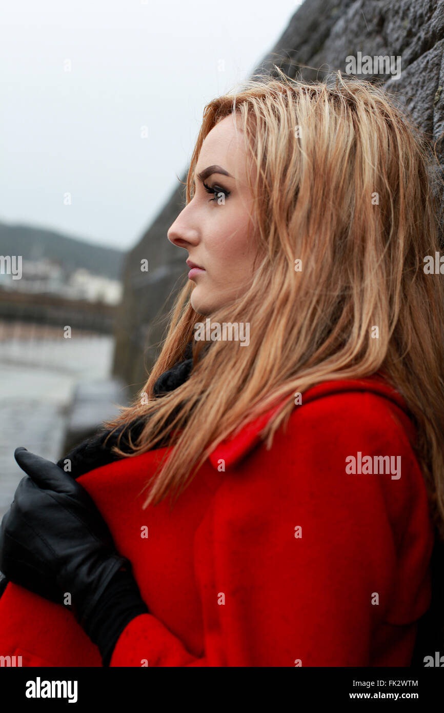 Profil d'une jeune femme portant un manteau rouge appuyée contre un vieux  mur de pierre Photo Stock - Alamy