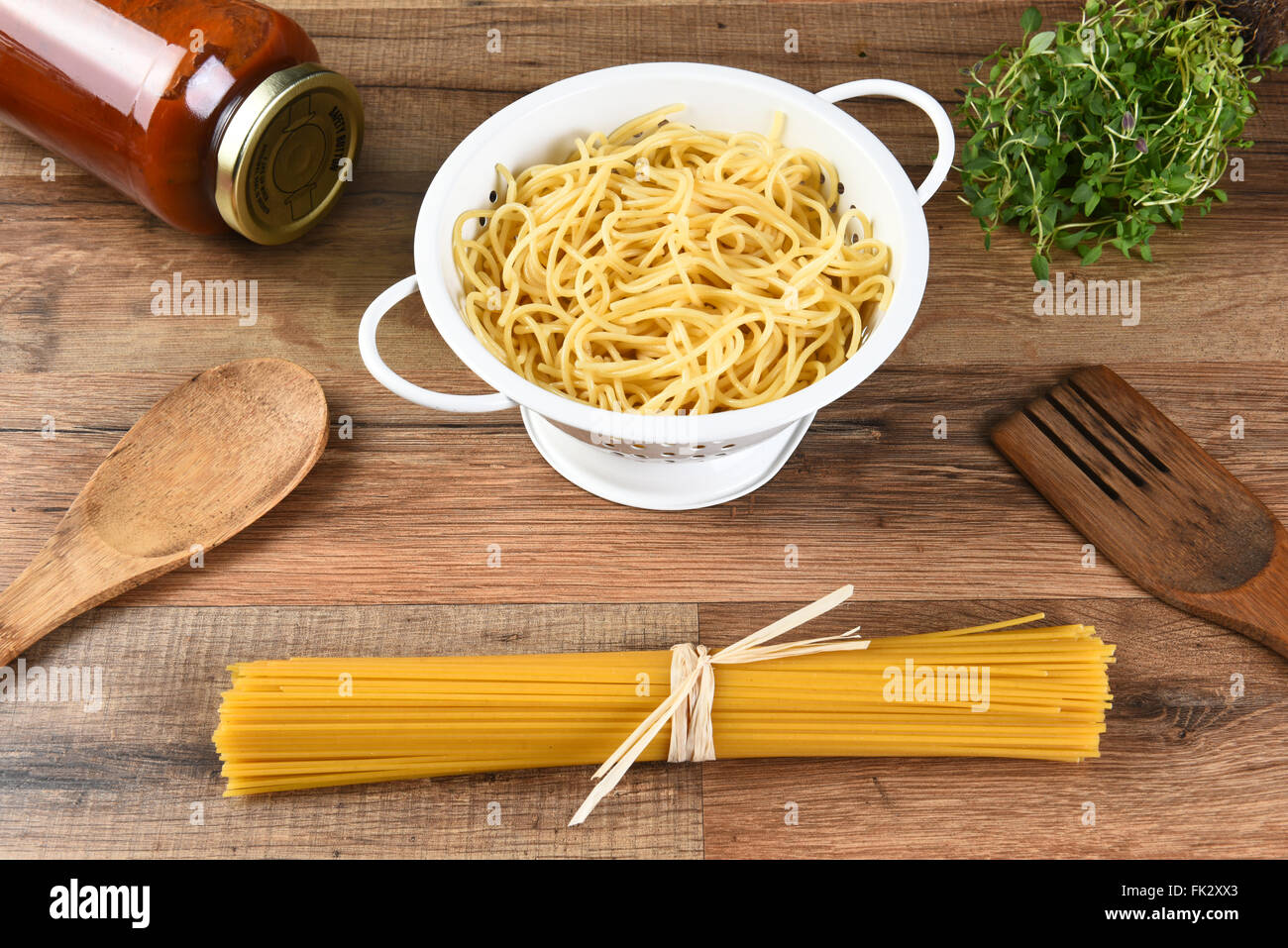 Still Life de spaghetti, pâtes cuites dans une passoire, un pot de sauce, des herbes et des outils. Banque D'Images