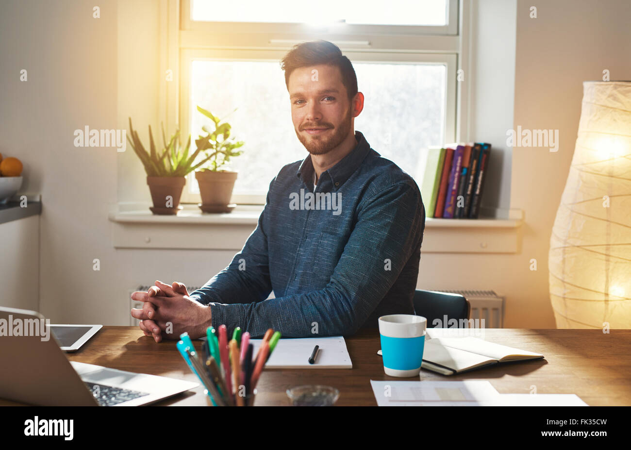 Homme assis à son bureau, dans son bureau à domicile pensée comme il regarde la caméra avec une expression pensive Banque D'Images