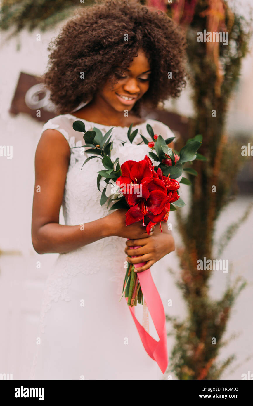 Belle mariée africaine souriant joyeusement avec bouquet de fleurs rouge dans les mains Banque D'Images