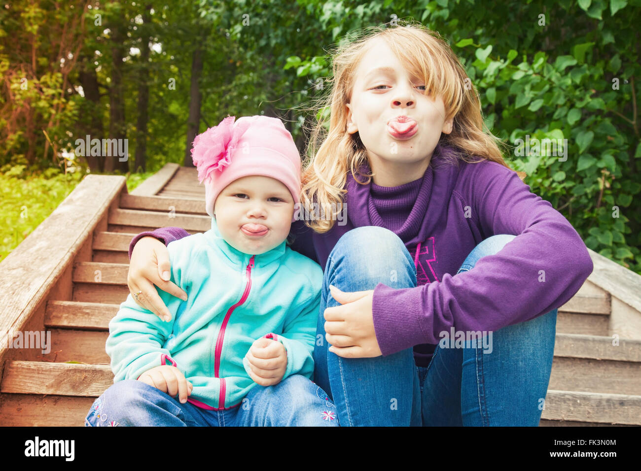 Drôle de petit blond Caucasian soeurs montrent des langues. Portrait en extérieur avec correction tonale effet filtre photo Banque D'Images