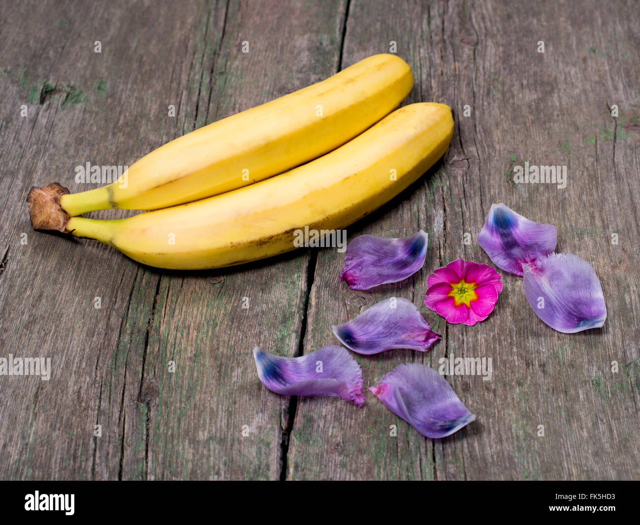 Deux bananes décoré avec une fleur rose et pétales de lilas sur une table en bois Banque D'Images