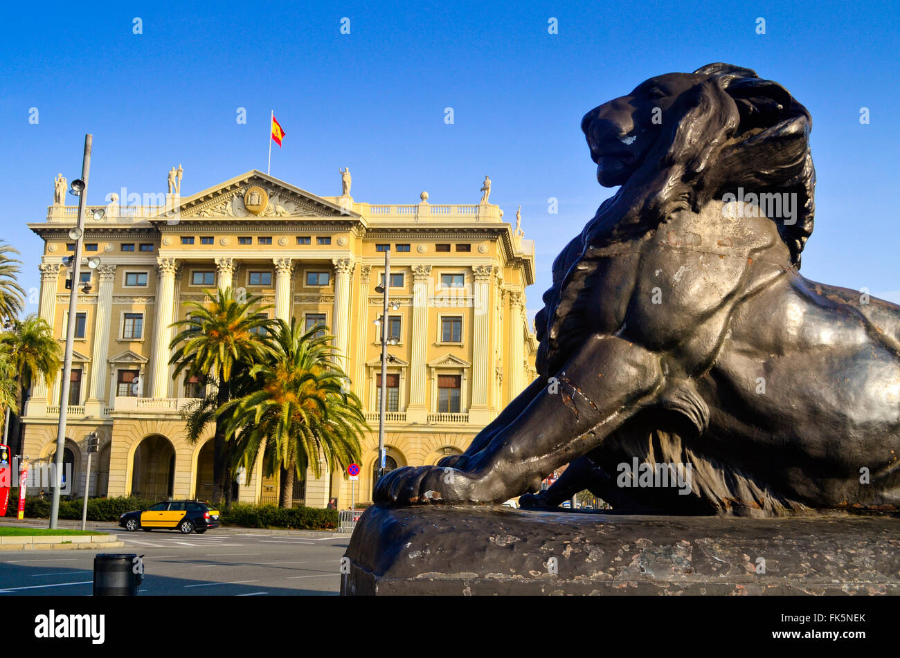 Lion de bronze à la base du monument de Christophe Colomb avec la Comandancia bâtiment en arrière-plan. Barcelone, Catalogne, Espagne. Banque D'Images