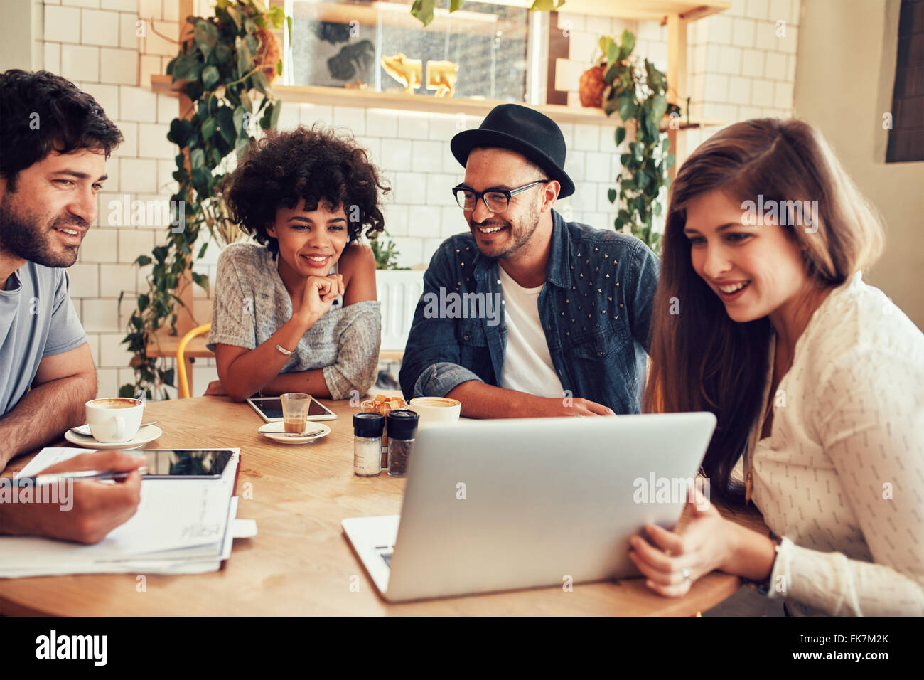 Groupe d'amis dans un café avec un ordinateur portable parmi eux. Heureux les jeunes gens assis au restaurant using laptop Banque D'Images