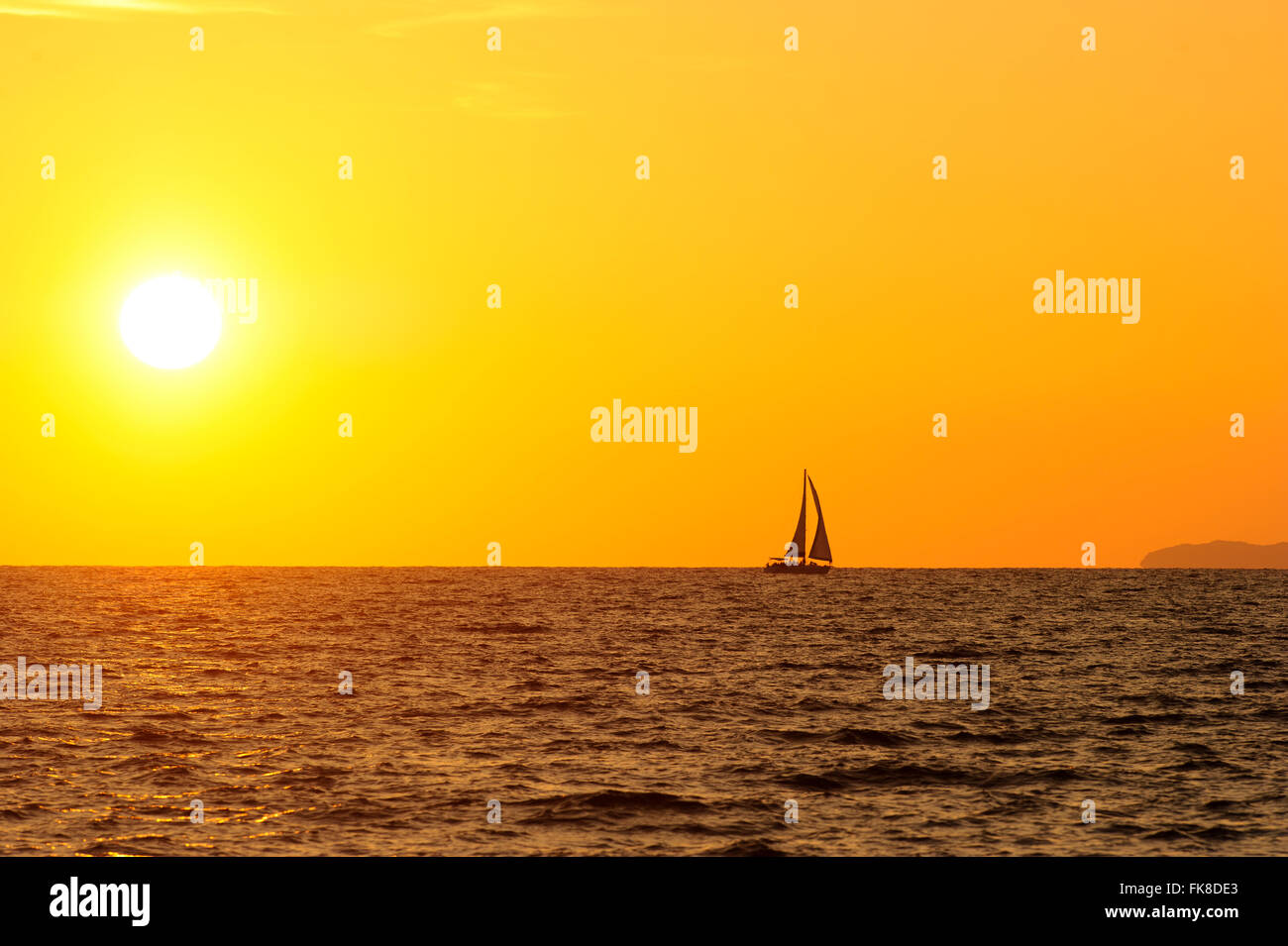 Voilier coucher du soleil est la silhouette d'un voilier avec un blanc chaud brûlant de soleil sur l'océan horizon contre un ciel orange. Banque D'Images